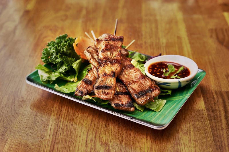 Thai street food dishes in NYC featuring grilled skewers with dipping sauce and fresh greens